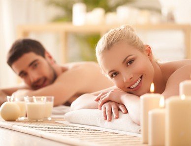A man and woman enjoying a relaxing massage on a massage table surrounded by flickering candles, creating an atmosphere of natural calm.
