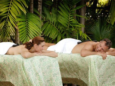 In home mobile massage with a man and woman relaxing on a massage table in a tropical setting.