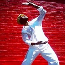 A man is dancing in front of a red brick wall.